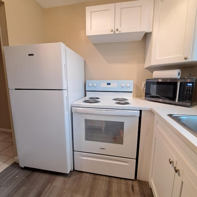 kitchen with white appliances, wood finished floors, a sink, light countertops, and white cabinetry