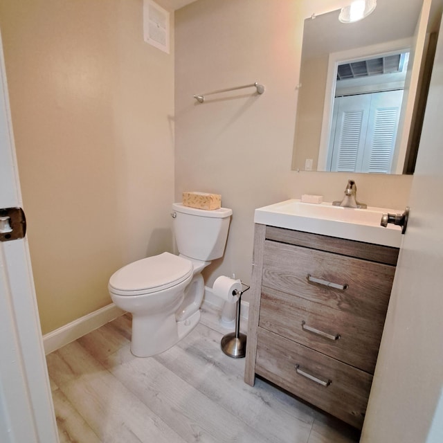 half bathroom with vanity, wood finished floors, visible vents, baseboards, and toilet