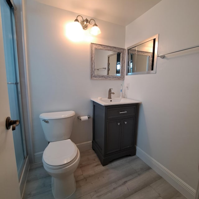 bathroom with toilet, vanity, baseboards, and wood finished floors