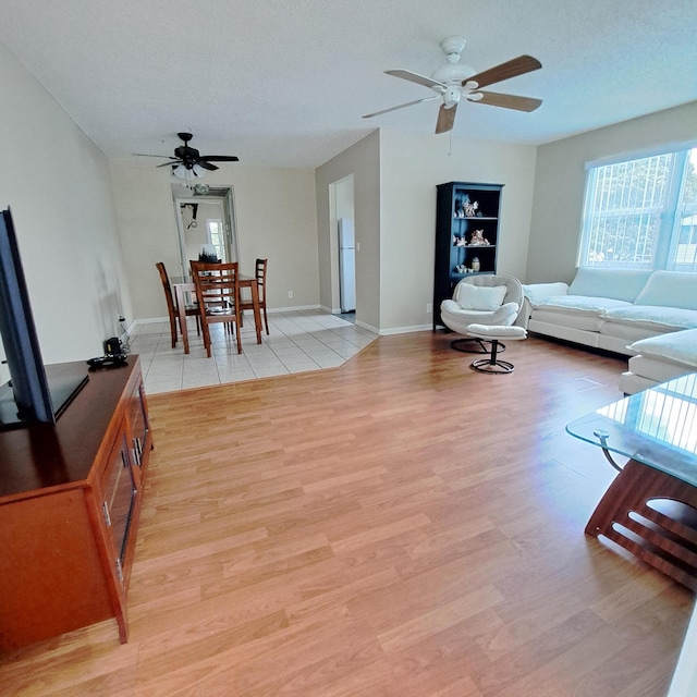 living area with baseboards, a ceiling fan, light wood-type flooring, and a textured ceiling