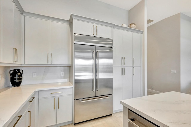 kitchen with decorative backsplash, light stone counters, and stainless steel built in refrigerator