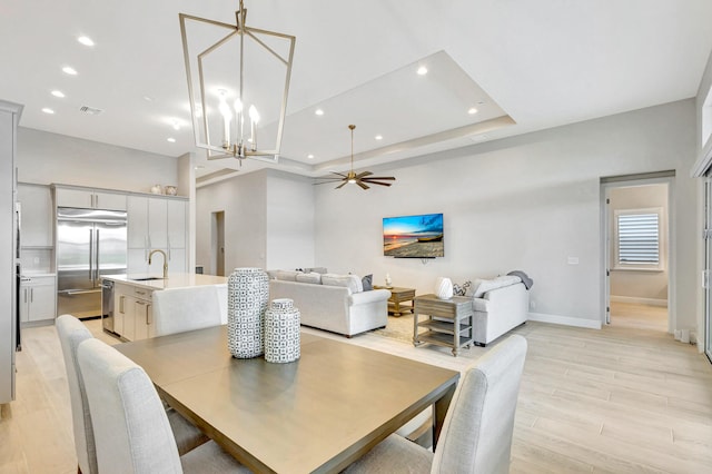 dining area featuring a tray ceiling, light hardwood / wood-style flooring, ceiling fan with notable chandelier, and sink