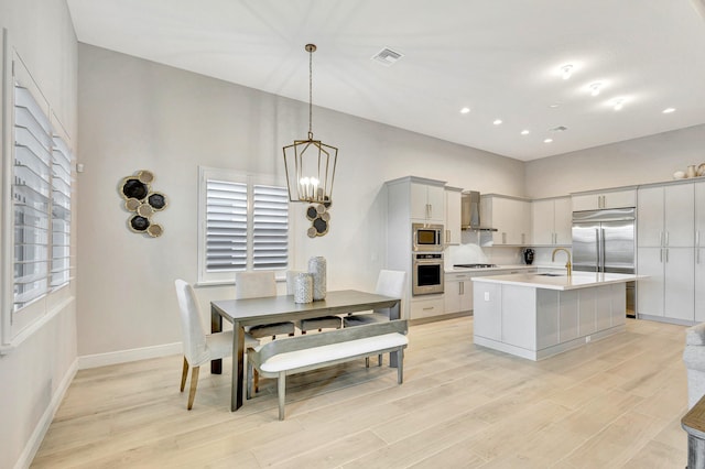 kitchen with sink, wall chimney range hood, pendant lighting, built in appliances, and a center island with sink