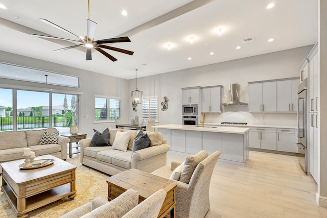 living room with ceiling fan with notable chandelier, light wood-type flooring, and sink