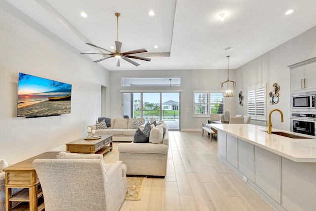 living room with ceiling fan with notable chandelier, light hardwood / wood-style floors, and sink