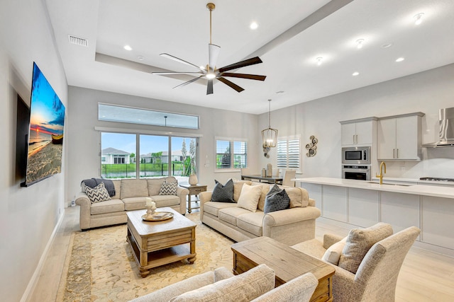 living room featuring ceiling fan with notable chandelier, light wood-type flooring, and sink