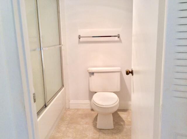 bathroom featuring bath / shower combo with glass door, toilet, and tile patterned floors