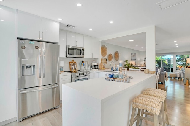 kitchen featuring a breakfast bar, white cabinets, kitchen peninsula, light hardwood / wood-style flooring, and stainless steel appliances