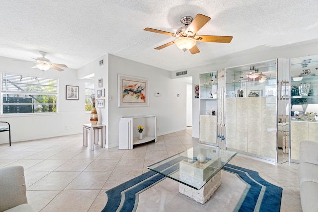 living room featuring a textured ceiling, light tile patterned floors, and ceiling fan