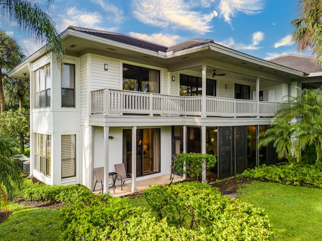 rear view of house featuring a balcony, ceiling fan, a lawn, and a patio area