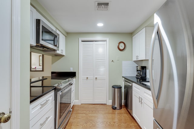 kitchen with light wood-type flooring, appliances with stainless steel finishes, white cabinetry, and decorative backsplash