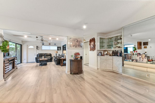 living room with a textured ceiling, ceiling fan, and light wood-type flooring