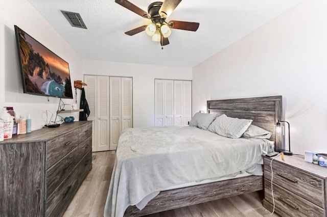 bedroom with light wood-type flooring, a textured ceiling, two closets, and ceiling fan