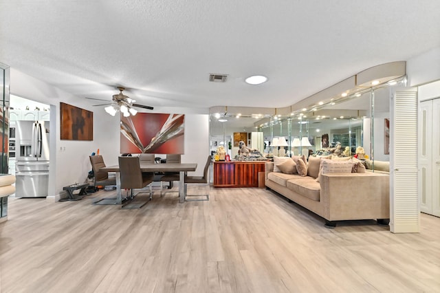 living room with a textured ceiling, light hardwood / wood-style flooring, and ceiling fan