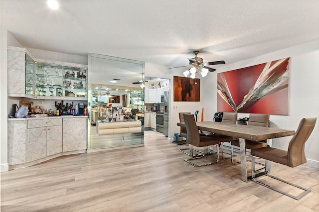 dining area featuring light wood-type flooring, a textured ceiling, indoor bar, and ceiling fan