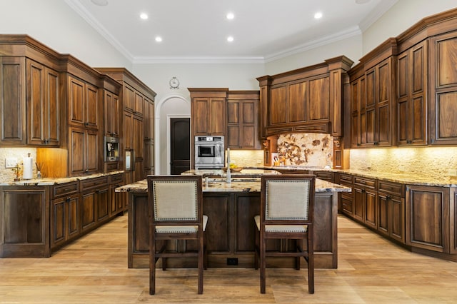 kitchen featuring an island with sink, light hardwood / wood-style flooring, ornamental molding, and tasteful backsplash