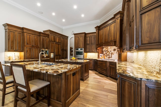 kitchen featuring a large island, light stone counters, light hardwood / wood-style floors, sink, and ornamental molding