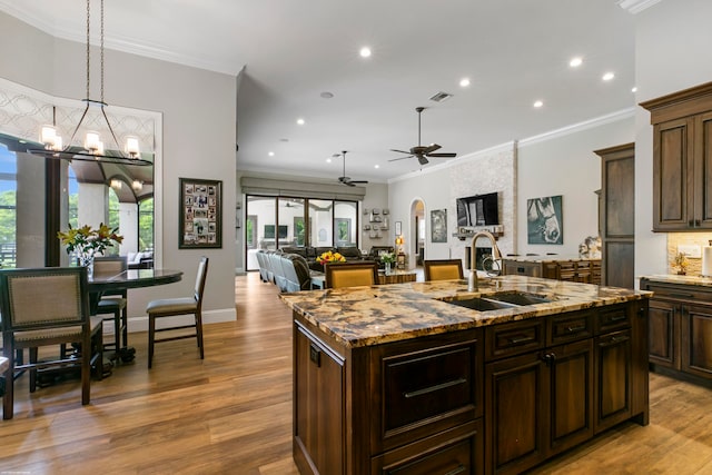 kitchen with light wood-type flooring, ornamental molding, sink, and an island with sink