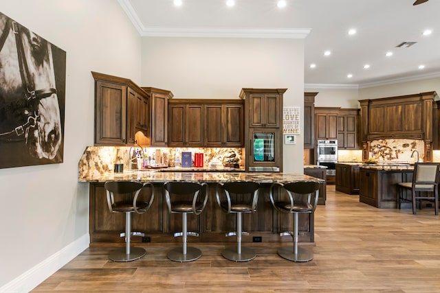 kitchen with crown molding, a kitchen bar, light stone countertops, and light hardwood / wood-style flooring