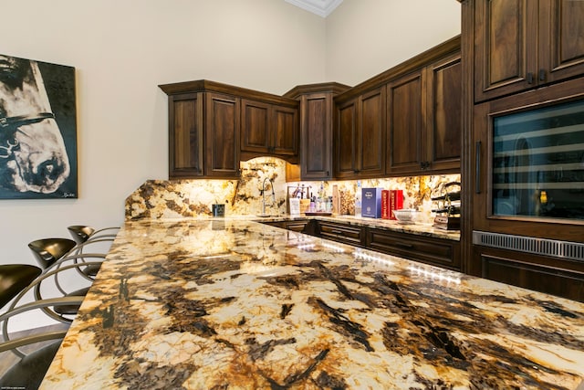 kitchen with ornamental molding, decorative backsplash, a kitchen bar, and dark brown cabinets