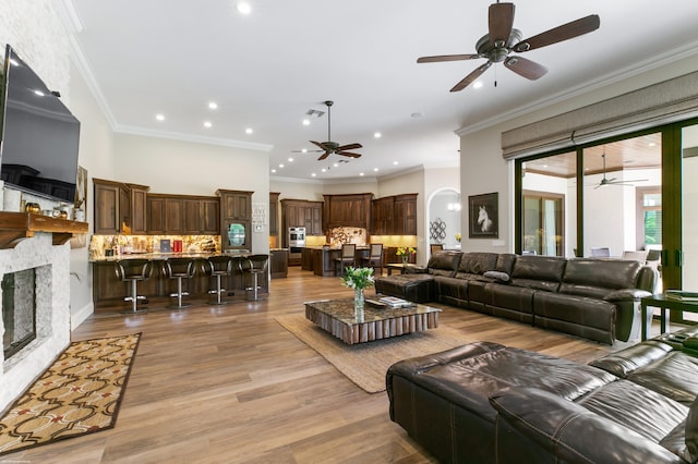 living room featuring light wood-type flooring, a fireplace, ornamental molding, and ceiling fan