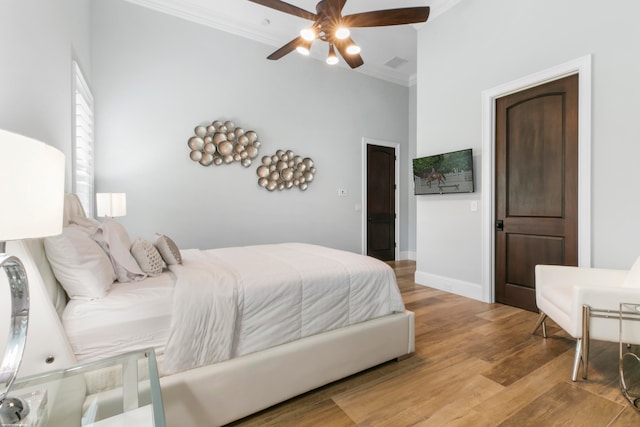 bedroom with ceiling fan, light wood-type flooring, a towering ceiling, and ornamental molding