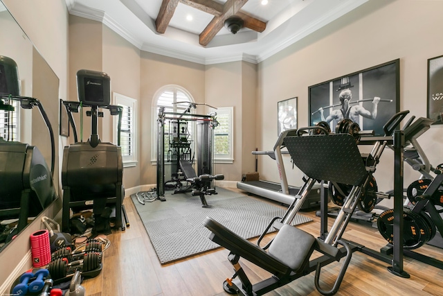 workout area featuring coffered ceiling, light hardwood / wood-style flooring, a towering ceiling, and crown molding