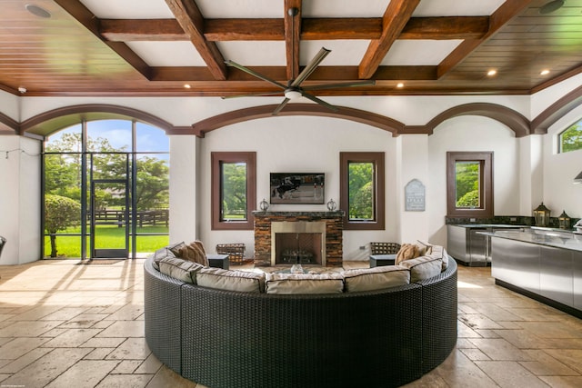 living room featuring ornamental molding, a stone fireplace, coffered ceiling, and beamed ceiling