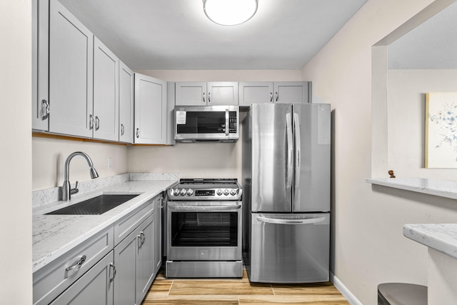 kitchen featuring gray cabinetry, appliances with stainless steel finishes, light stone counters, light hardwood / wood-style floors, and sink