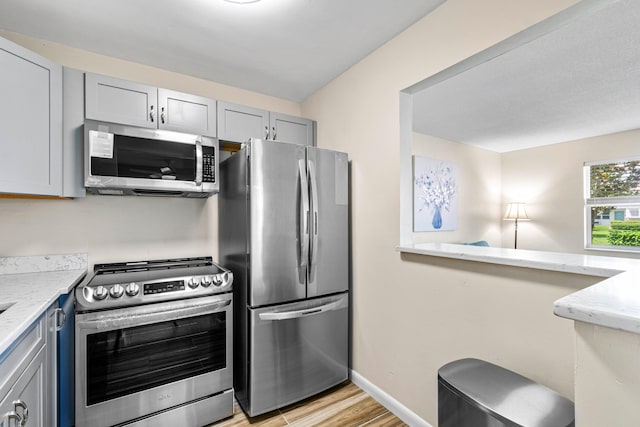 kitchen featuring light wood-type flooring, appliances with stainless steel finishes, gray cabinets, and light stone countertops