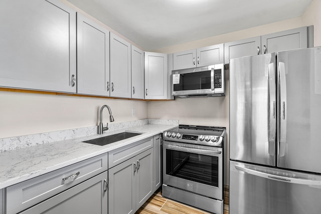 kitchen featuring light wood-type flooring, gray cabinets, stainless steel appliances, light stone counters, and sink