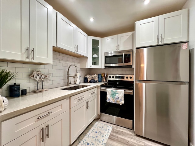 kitchen featuring sink, light hardwood / wood-style flooring, white cabinetry, stainless steel appliances, and light stone countertops