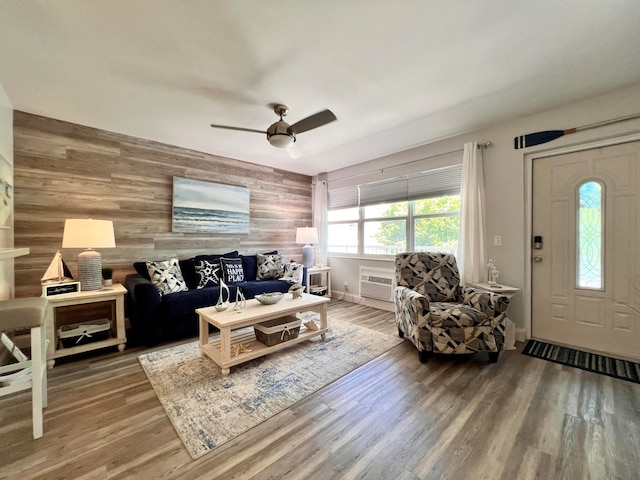 living room featuring an AC wall unit, wooden walls, ceiling fan, and wood-type flooring