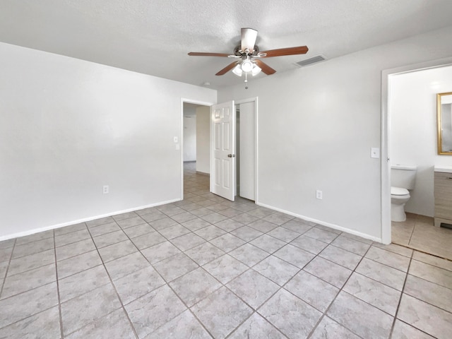 unfurnished bedroom with ensuite bath, a textured ceiling, light tile patterned floors, and ceiling fan