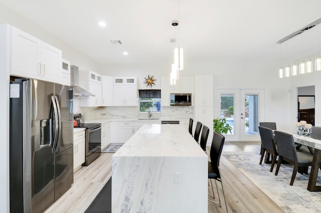 kitchen with white cabinets, a center island, appliances with stainless steel finishes, sink, and wall chimney range hood