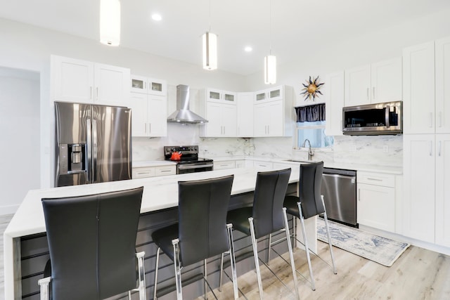 kitchen featuring a kitchen bar, a kitchen island, stainless steel appliances, and wall chimney exhaust hood