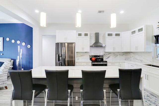 kitchen featuring a center island, stainless steel appliances, light stone counters, and wall chimney range hood