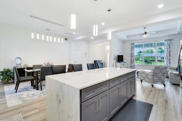 kitchen featuring decorative light fixtures, light hardwood / wood-style flooring, a center island, gray cabinets, and ceiling fan