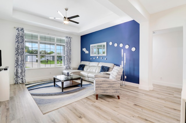 living room featuring a raised ceiling, ceiling fan, and light wood-type flooring