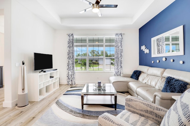 living room with ceiling fan, light wood-type flooring, and a tray ceiling