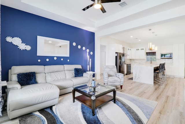 living room featuring ceiling fan with notable chandelier and light hardwood / wood-style flooring