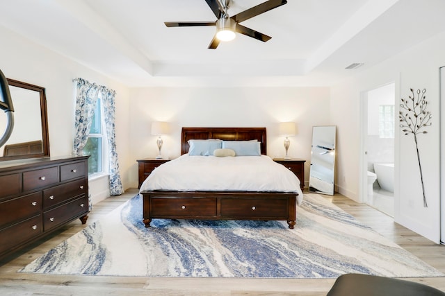 bedroom featuring light wood-type flooring, a tray ceiling, ceiling fan, and ensuite bathroom