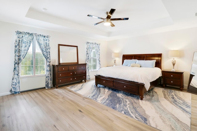 bedroom with a tray ceiling, light hardwood / wood-style floors, and ceiling fan