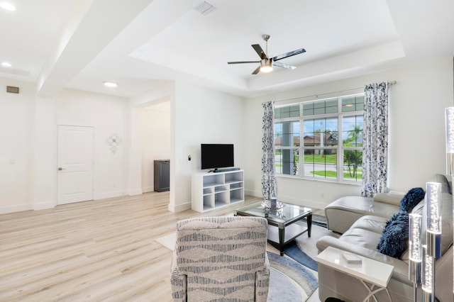 living room featuring a tray ceiling, ceiling fan, and light hardwood / wood-style flooring