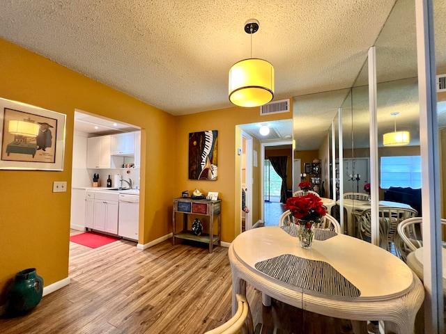 dining space featuring sink, light hardwood / wood-style flooring, and a textured ceiling