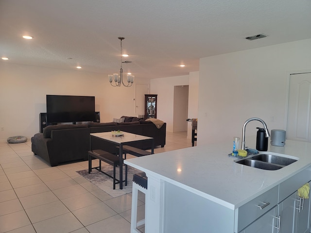 kitchen with a notable chandelier, a textured ceiling, light tile patterned floors, an island with sink, and sink