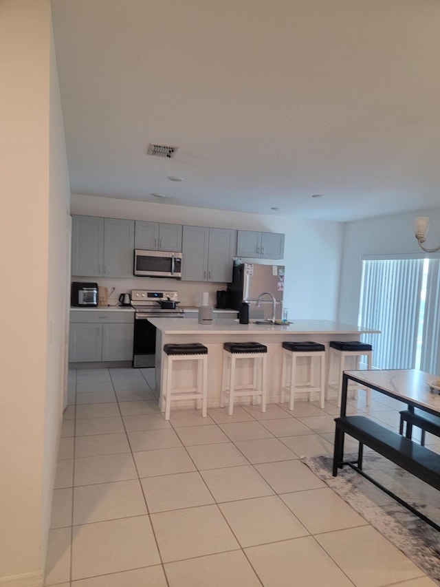 kitchen with gray cabinets, light tile patterned floors, stainless steel appliances, and a breakfast bar