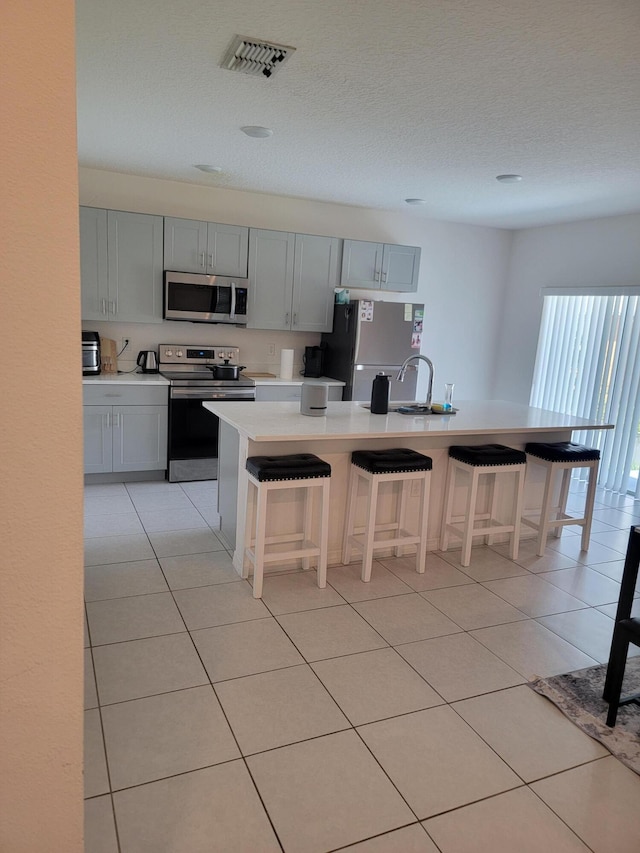 kitchen featuring a center island with sink, a breakfast bar, stainless steel appliances, and gray cabinets