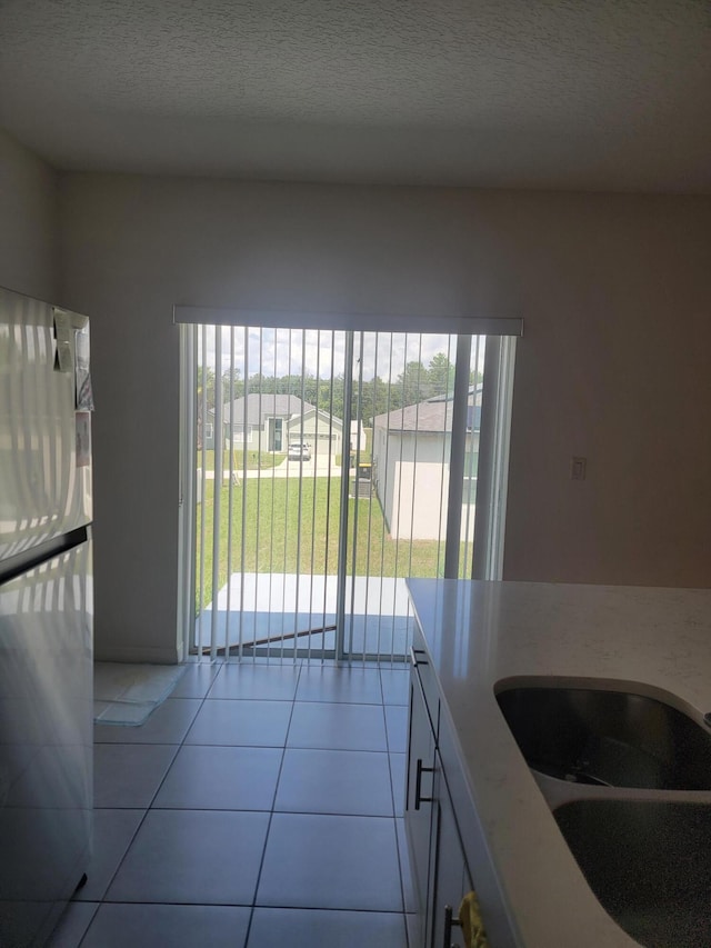 kitchen with a wealth of natural light, stainless steel refrigerator, light tile patterned floors, and sink