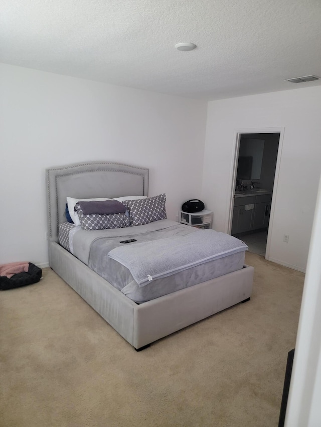 bedroom with a textured ceiling, light colored carpet, ensuite bath, and sink